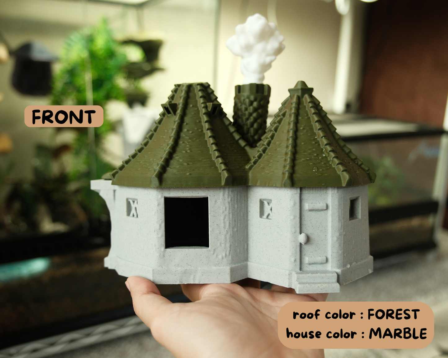 Small model house with a forest roof and marble body held by a hand.
